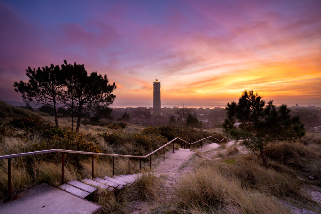 Tegen een opkomende zon boven de Waddenzee, het dorp West Terschelling en haar vuurtoren, foto gemaakt vanaf een hoog duin.Brandaris West-Terschelling © Marjolein van Roosmalen