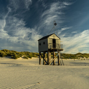 Het iconische drenkelingenhuisje op het strand nabij paal 19 op Terschelling, foto genomen vanaf het strand, tevens duin en sluierbewolking te zine tegen een blauwe lucht. Terschelling © Marjolein van Roosmalen